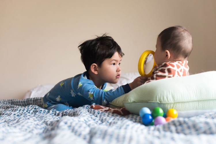 A toddler using a magnifying glass to examine his newborn baby sibling