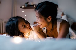 A mom and daughter lying in bed talking and laughing while the kid spills the tea about their life