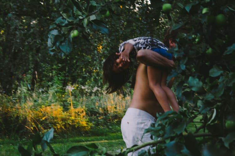 A dad holding his daughter over his shoulder playing with her in the forest