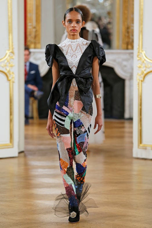 A model walking the runway in a Yolancris design featuring a white top, black jacket and multicolore...