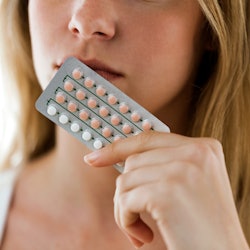 A blonde woman holding a package of birth control pills near to her lips