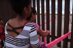 A little kid playing on a bright pink seesaw at one side of border
