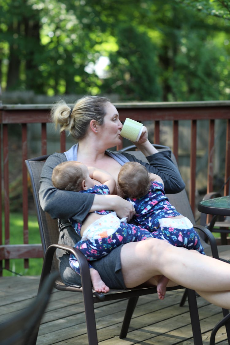 photo of mom breastfeeding twins sitting on back deck and drinking coffee