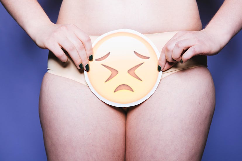 A woman wearing pale-yellow panties holding a sad-looking emoji sticker over her private parts