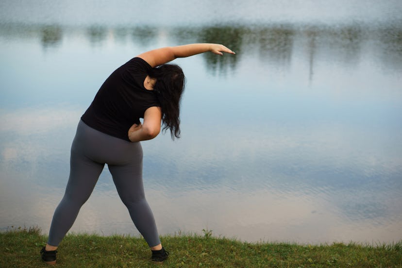 A woman in her gym clothes stretching with a lake in front of her
