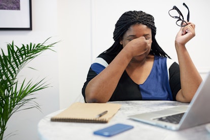 A woman taking her glasses off and crying in her office 