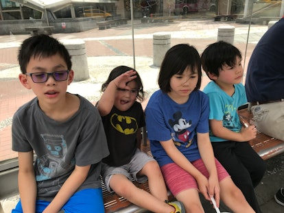 Four kids sitting on a bus station bench