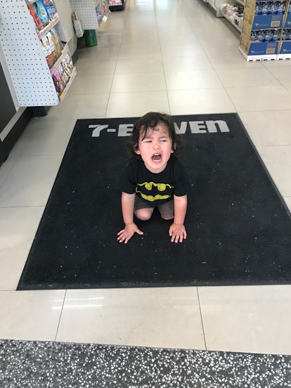 A little kid in Batman shirt sitting on a shop floor and screaming