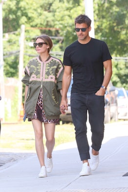 Olivia Palermo in a leopard skirt and long light green jacket holding hands with her partner 