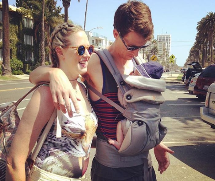 A man with a baby in a baby carrier and his wife who gave birth but still has a pregnancy-resembling...