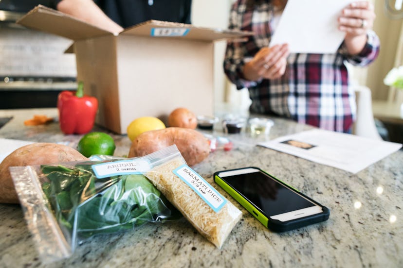 A man and a woman opening a meal subscription box and its content next to it