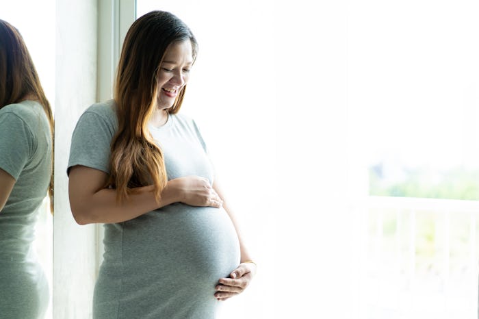 woman smiling holding pregnant belly by window
