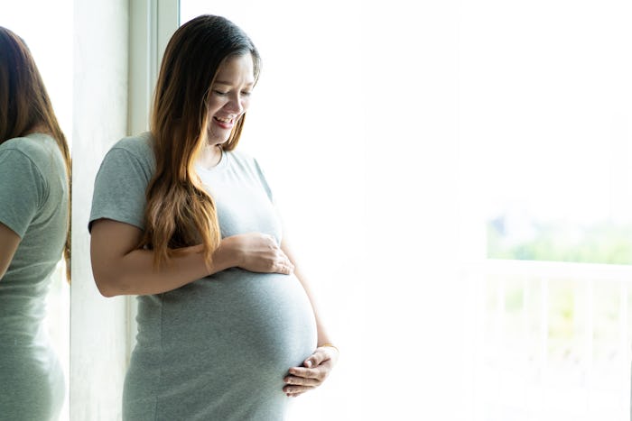 woman smiling holding pregnant belly by window