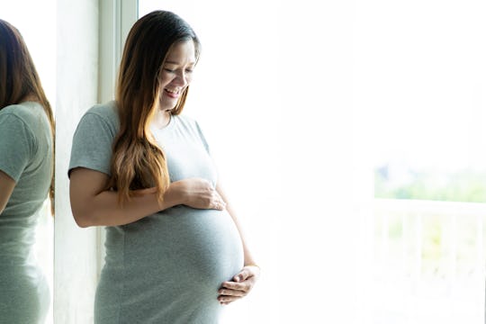 woman smiling holding pregnant belly by window