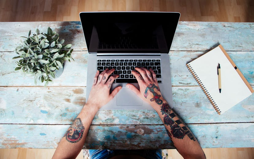 A person with tattooed hands typing on a laptop, working from home