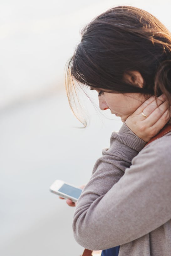 A woman in a beige sweater holding a smartphone, and swiping on a dating app