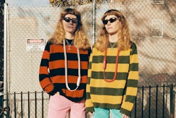 Two women in front of a chainlink fence in matching cool girl outfits, sunglasses, striped sweaters ...