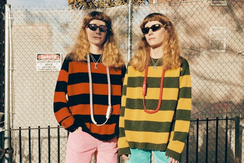 Two women in front of a chainlink fence in matching cool girl outfits, sunglasses, striped sweaters ...