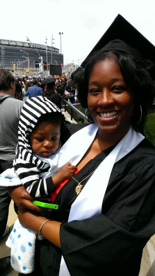 A mom wearing a graduation cap and gown, holding her child in a stripy hoodie 