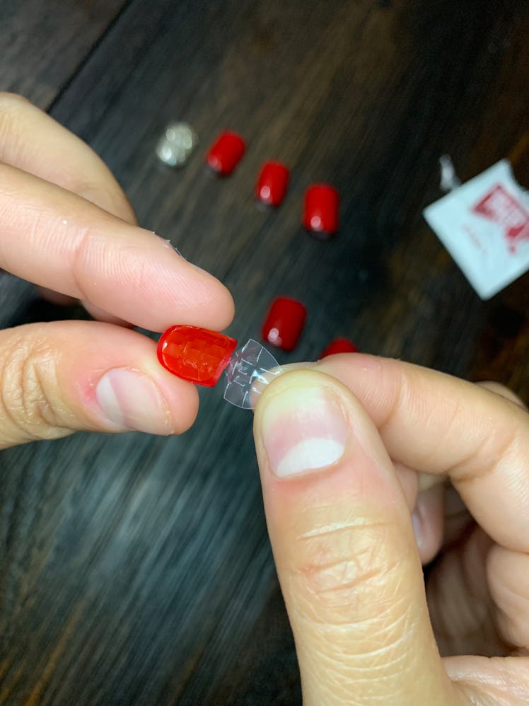 A closeup of fingers removing the safety plastic from a red press-on nail 