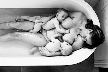 beautiful black and white photo of mom breastfeeding twins in the tub