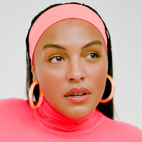 A brunette woman with a pink headband, pink turtleneck, and peach hoop earrings