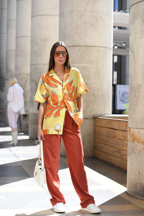 A woman posing in a hawaiian shirt, red pants and white sneakers
