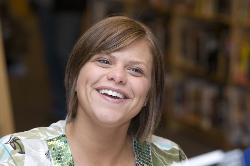 Jade Goody smiling off camera in a floral shirt in the library