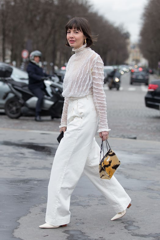 A woman in a tulle sweater and white baggy denim pants