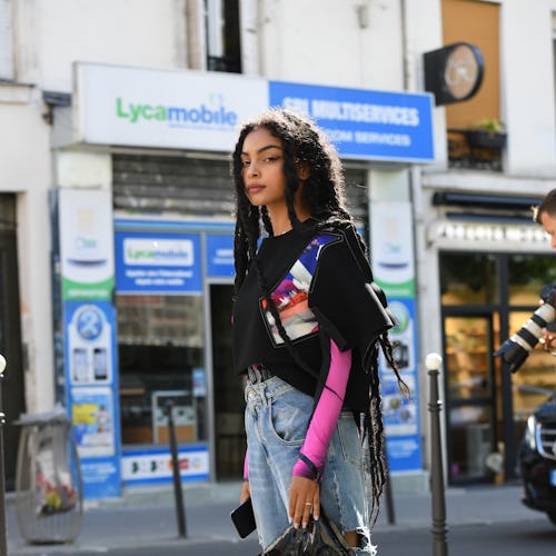 A woman in a black shirt with pink sleeves, baggy denim jeans, black boots and a black bag