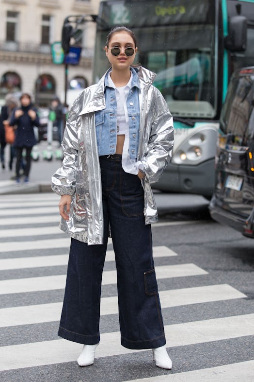 A woman in a white top, denim shirt, silver jacket, and baggy black pants