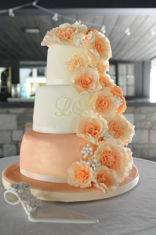 A peach colored three layer wedding cake with flowers piped on the side