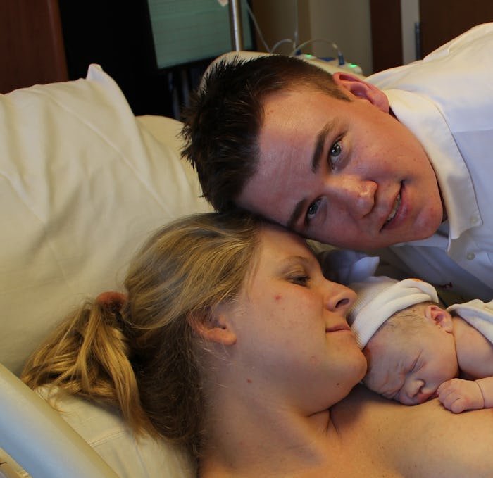 Crystal Henry lying in a hospital bed with her newborn baby on her chest and her husband next to her