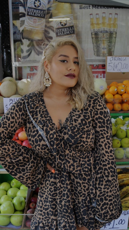 Queer Latina activist Veggie Mijas in front of a store with veggies and fruits in the background