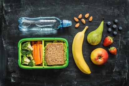 A lunch box with a sandwich and veggies, a banana, a pear, an apple, strawberries, blueberries, almo...