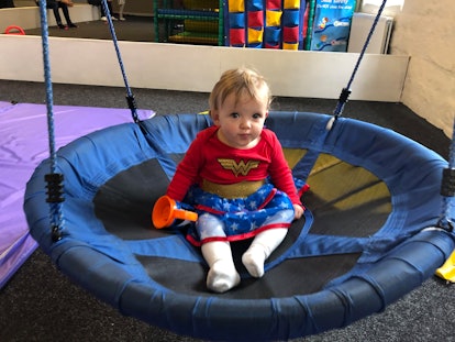 A toddler girl dressed in a Wonder Woman costume sitting on a trampoline