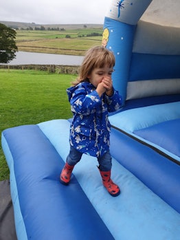 A girl in a blue raincoat and red rubber boots standing on the inflatable castle