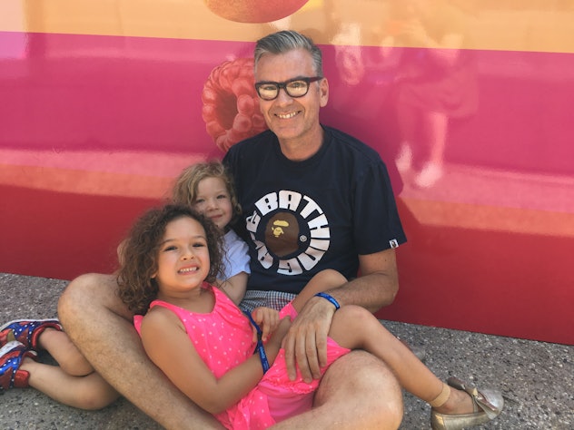 Simon with glasses and a tee holding his two daughters in his lap 