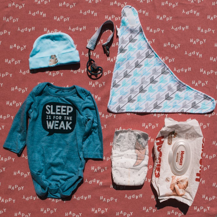 A onesie, a bib, a baby hat, wet wipes and a diaper from a mom's bag 