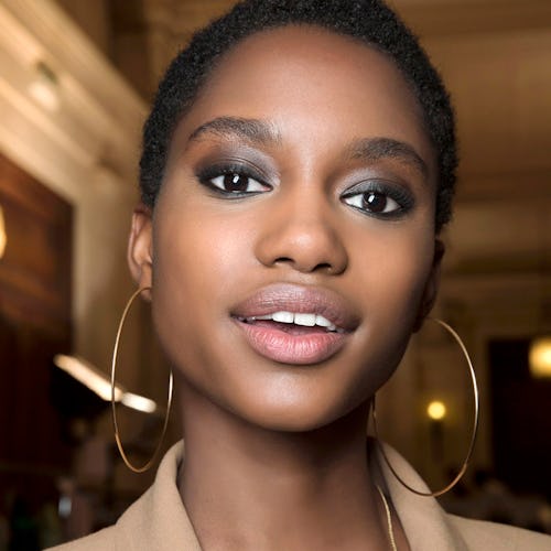 A model wearing eyeshadow available at Ulta, with a beige blazer and large hoop earrings 
