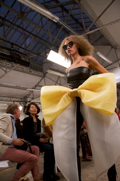 The model wears a leather top with a supersized yellow and white bow by Kimhékim