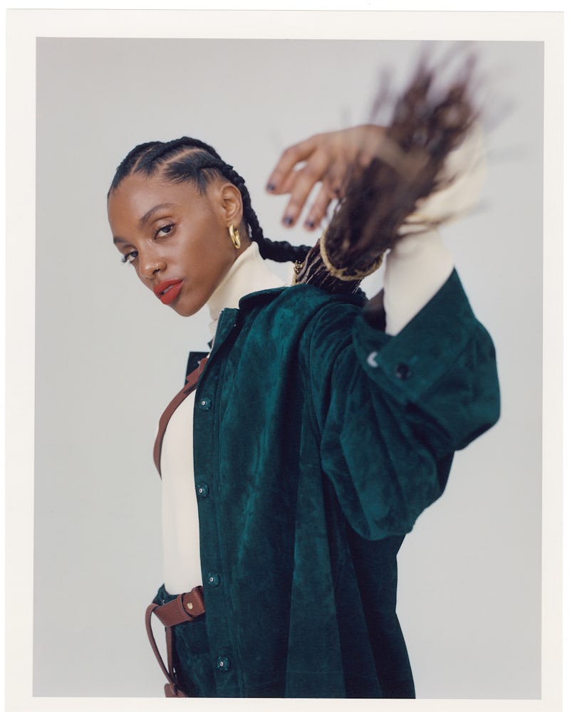 Mereba posing with a broom while wearing an emerald green Jil Sander's oversized shirt, a white knit...