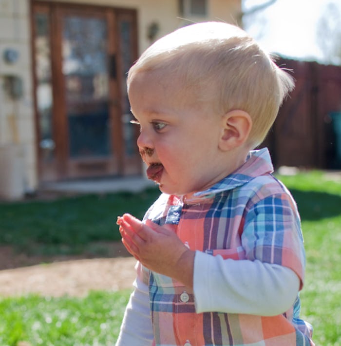 A toddler standing outside putting something gross in his mouth