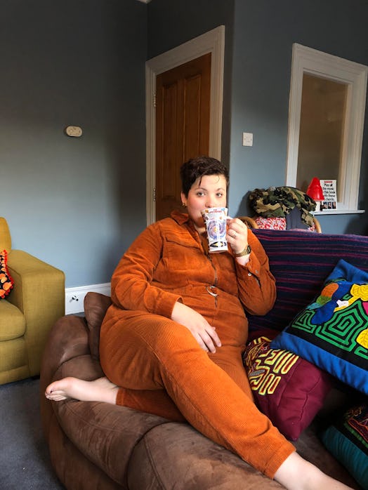 Marie Southard Ospina, in an orange velvet tracksuit, sitting on a couch and drinking from a mug
