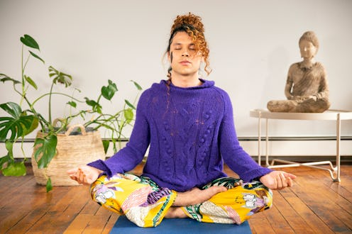 A person meditating while doing yoga in front of a buddha statue and next to a potted house plant
