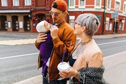 A woman with short blonde hair looking at her partner carrying their baby while walking the street