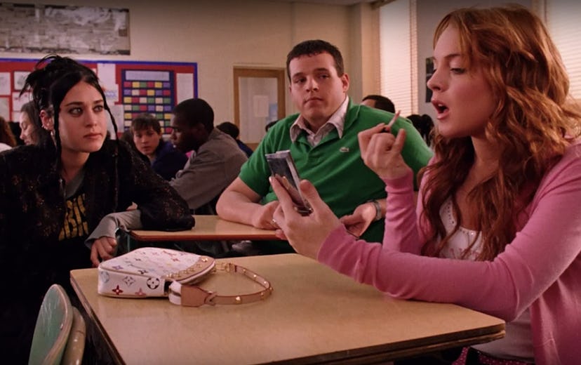 Lindsay Lohan sitting in school in “Mean Girls” while a white pochette is on her desk 