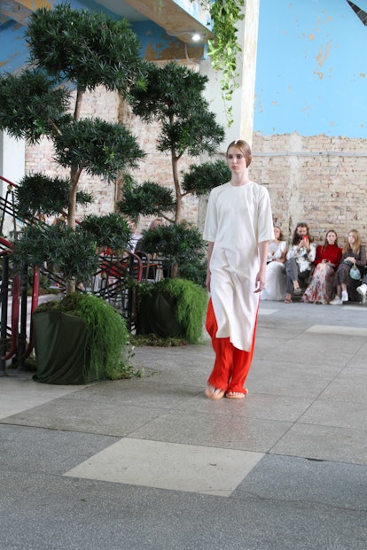 A model wearing ukranian brands walking down the street in a long white top and red pants