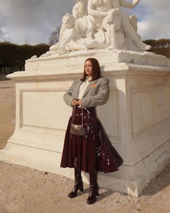 A model wearing a white shirt, a grey blazer, a brown vinyl skirt, a brown bag and brown boots