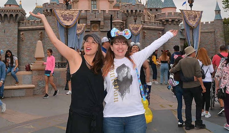 Two sisters wearing Mickey Mouse ears stand in front of Sleeping Beauty's Castle at Disneyland with ...